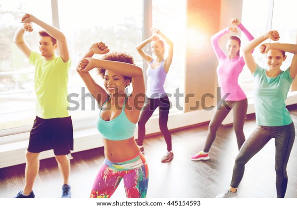 fitness, sport,\
dance and lifestyle concept - group of smiling people with coach\
dancing zumba in gym or\
studio