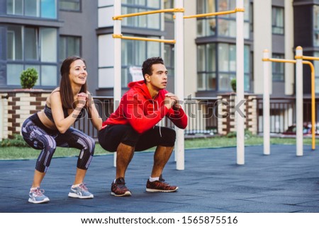 fitness, sport, exercise, training and lifestyle concept - mixed race young man and woman doing squatting exercise on street sports ground. Staying fit and healthy concept