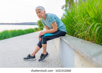 Fitness, sport, exercising and healthy lifestyle concept - Mature woman with injured knee or leg outdoors. Knee injury for senior woman athlete runner. - Powered by Shutterstock