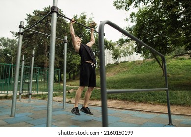 Fitness, sport, exercising, training and lifestyle concept - young man doing pull ups on horizontal bar outdoors. Sporty man working out in outdoor gym in park. - Powered by Shutterstock