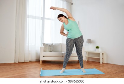 Fitness, Sport, Exercising, Training And Lifestyle Concept - Smiling Plus Size Woman Stretching On Mat At Home