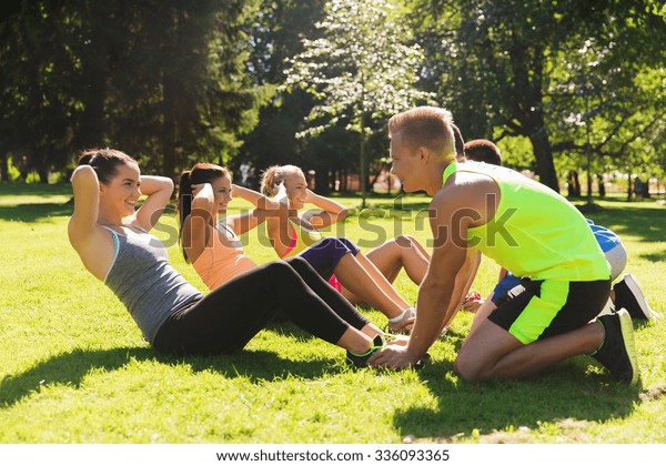 fitness, sport, friendship and healthy lifestyle\
concept - group of happy teenage friends or sportsmen exercising\
and doing sit-ups at boot\
camp