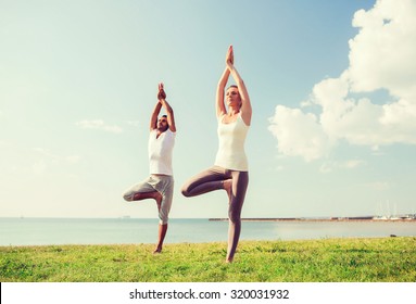 fitness, sport, friendship and lifestyle concept - smiling couple making yoga exercises outdoors