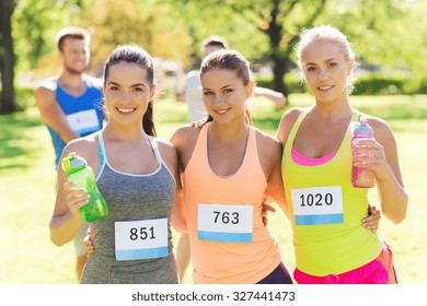 fitness, sport, friendship, marathon and healthy lifestyle concept - happy young sporty women with racing badge numbers and water bottles outdoors - Powered by Shutterstock