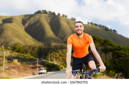 Fitness, Sport And Healthy Lifestyle Concept - Happy Young Man Riding Bicycle Over Big Sur Hills And Road Background In California