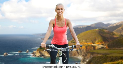 Fitness, Sport And Healthy Lifestyle Concept - Happy Young Woman Riding Bicycle Over Big Sur Hills And Pacific Ocean Background In California