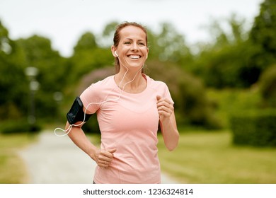 fitness, sport and healthy lifestyle concept - smiling woman with earphones wearing armband for smartphone, jogging at summer park and listening to music - Powered by Shutterstock