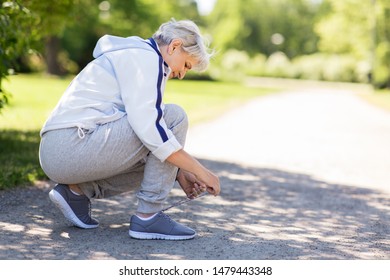 fitness, sport and healthy lifestyle concept - senior woman tying shoe laces at summer park - Powered by Shutterstock