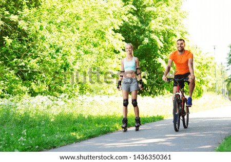 fitness, sport and healthy lifestyle concept - happy couple with rollerblades and bicycle riding in summer park