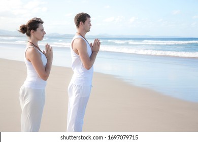 Fitness, Sport & Lifestyle Concept - Man And Woman Doing Yoga Prayer Pose On The Beach, Wearing All White