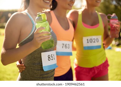 fitness, sport marathon and healthy lifestyle concept - close up of happy young sporty women with bottles of water and racing badge numbers on shirts - Powered by Shutterstock