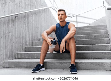 Fitness, Sport And People Concept - Tired Young Man With Protein Shake In Bottle Sitting On Stairs