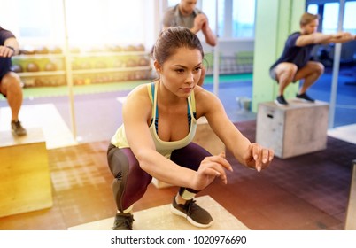 fitness, sport, people and exercising concept - woman doing box jumps at group training in gym
