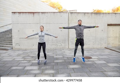 Fitness, Sport, People, Exercising And Lifestyle Concept - Happy Man And Woman Doing Jumping Jack Or Star Jump Exercise Outdoors