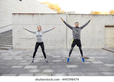 Fitness, Sport, People, Exercising And Lifestyle Concept - Happy Man And Woman Doing Jumping Jack Or Star Jump Exercise Outdoors