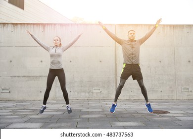 Fitness, Sport, People, Exercising And Lifestyle Concept - Happy Man And Woman Doing Jumping Jack Or Star Jump Exercise Outdoors