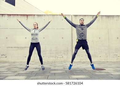 Fitness, Sport, People, Exercising And Lifestyle Concept - Happy Man And Woman Doing Jumping Jack Or Star Jump Exercise Outdoors