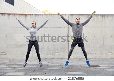 fitness, sport, people, exercising and lifestyle concept - happy man and woman doing jumping jack or star jump exercise outdoors