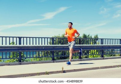 Fitness, Sport, People, Technology And Healthy Lifestyle Concept - Smiling Young Man With Heart Rate Watch Running At Summer Seaside