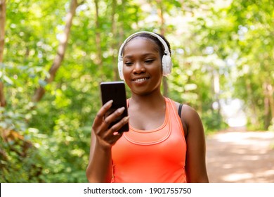 fitness, sport and technology concept - happy smiling young african american woman with headphones listening to music on smartphone outdoors - Powered by Shutterstock