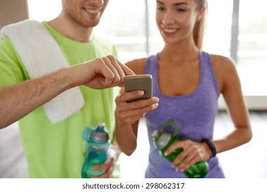 fitness, sport, technology and slimming concept - close up of smiling young woman and personal trainer with smartphone and water bottles in gym