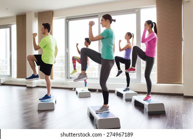 fitness, sport, training, aerobics and people concept - group of people working out with steppers in gym