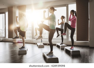 fitness, sport, training, aerobics and people concept - group of people working out with steppers in gym