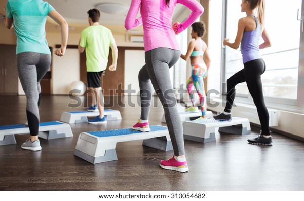 fitness,\
sport, training, aerobics and people concept - close up of people\
working out with steppers in gym from\
back
