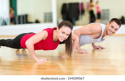 fitness, sport, training, gym and lifestyle concept - smiling couple doing push-ups in the gym