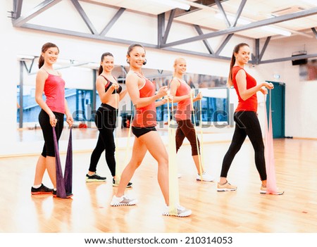fitness, sport, training, gym and lifestyle concept - group of smiling people with instructor working out with rubber bands in the gym