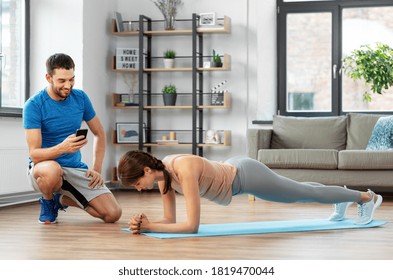 Fitness, Sport, Training And Lifestyle Concept - Happy Smiling Personal Trainer With Smartphone And Woman Doing Plank At Home
