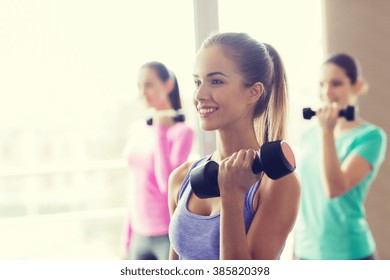 fitness, sport, training and lifestyle concept - group of happy women with dumbbells flexing muscles in gym - Powered by Shutterstock