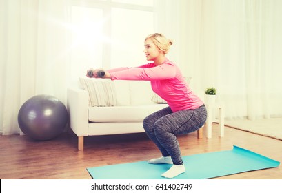 fitness, sport, training and lifestyle concept - smiling woman with dumbbells exercising and doing squats at home