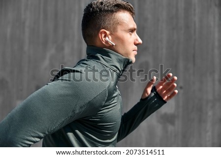 fitness, sport, training and lifestyle concept - young man with wireless earphones running outdoors