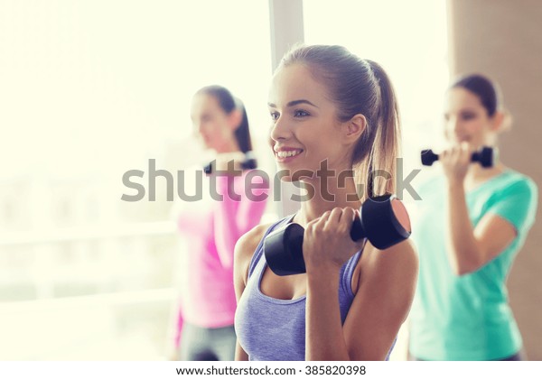 fitness, sport, training
and lifestyle concept - group of happy women with dumbbells flexing
muscles in gym