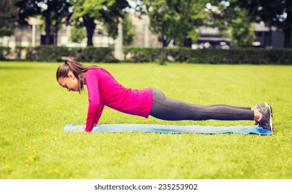 fitness, sport, training, park and lifestyle concept - smiling woman doing doing push-ups on mat outdoors
