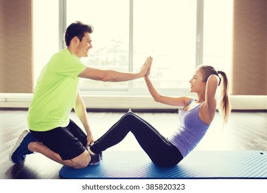 Fitness, Sport, Training, Teamwork And People Concept - Happy Woman With Personal Trainer Doing Sit Ups And High Five Gesture In Gym