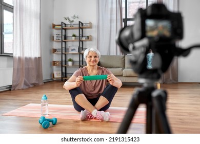 Fitness, Sport And Video Blogging Concept - Happy Senior Woman Or Blogger With Camera And Resistance Loop Streaming Online Class At Home