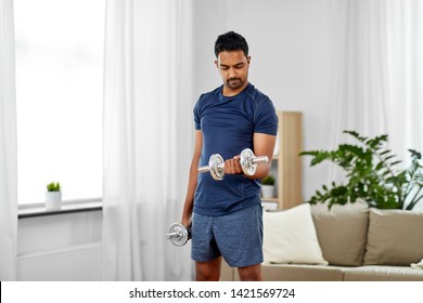 fitness, sport, weightlifting and bodybuilding concept - indian man exercising with dumbbells at home