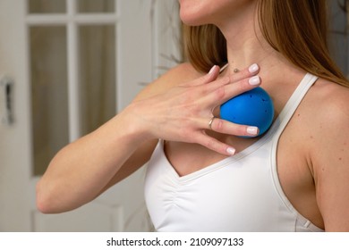 Fitness. A sports girl in a white T-shirt holds a blue massage gymnastic ball, pressing it to her chest with her hand. Close-up, the head is not visible.