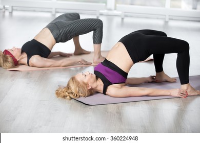 Fitness, stretching practice, group of two attractive fit mature women working out in sports club, "warming up", doing backbend, Setu Bandhasana Pose, shoulder bridge exercise in class, full length
