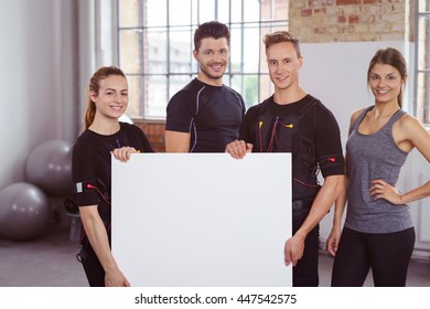 Fitness team in a ems gym with four smiling young people, two men and two women, holding a blank sign with copy space in front of them