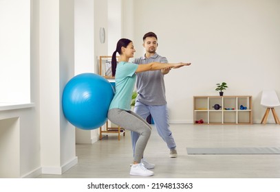 Fitness trainer helping young female patient do wall squats with blue fit ball to get rid of backache and regain spinal health. Woman doing back exercise in physio room of modern clinic - Powered by Shutterstock