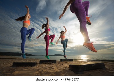 fitness, training, aerobics and people concept - group of girls working out with steppers on the beach (Focus on front female body)