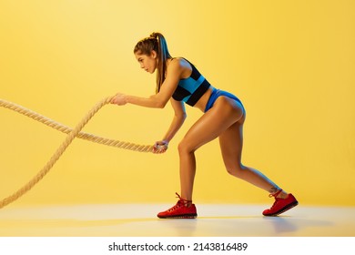 Fitness Training. Portrait Of Young Sportive Girl Workout With Sports Ropes Isolated On Yellow Studio Background. Female Sport, Action, Motion, Beauty And Health Lifestyle Concept. Copy Space For Ad