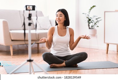 Fitness Vlog. Portrait of active asian woman filming video for her internet channel at social media, looking and talking to camera, sitting on the floor on yoga mat. Trainer recording tutorial at home - Powered by Shutterstock