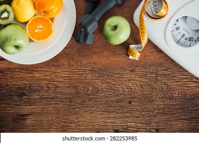 Fitness And Weight Loss Concept, Dumbbells, White Scale, Fruit And Tape Measure On A Wooden Table, Top View