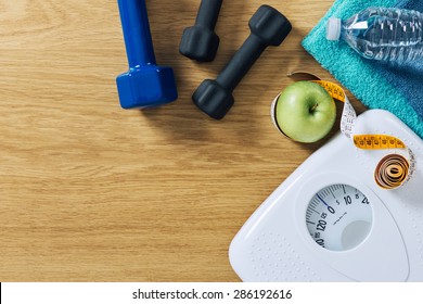 Fitness And Weight Loss Concept, Dumbbells, Tape Measure, White Scale Towels And Water Bottle On A Wooden Table, Top View