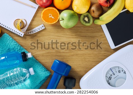 Fitness and weight loss concept, dumbbells, white scale, towels, fruit, tape measure and digital tablet on a wooden table, top view