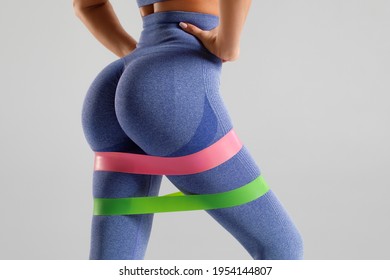 Fitness woman doing exercise for glutes with resistance band on gray background. Beautiful buttocks, athletic girl working out